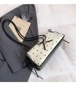 Detail of off-white pleated fabric shoulder bag with black bow and heart pendant charm