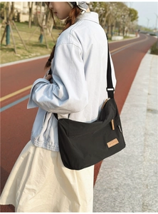 Detailed side view of a black waterproof nylon messenger bag worn by a person outdoors