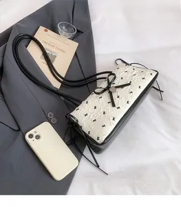Detail of cream pleated crossbody bag with black bow and silver heart pendant