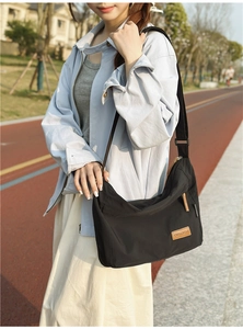 Detail of water-resistant black nylon messenger bag with brown leather brand label