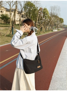 Outdoor shot of a black waterproof nylon messenger bag with a brown leather logo patch