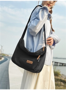 Side view of black nylon crossbody bag with zipper and logo patch worn by a model