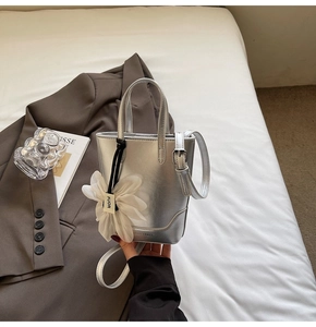 Détail d'un sac seau argenté avec breloque fleur blanche et poignée texturée