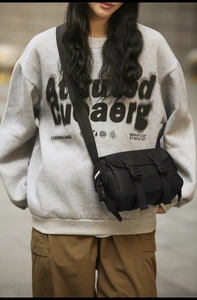 Detail of black nylon messenger bag with buckle closure worn with casual streetwear style