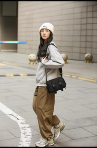Outdoor street style view of a black nylon messenger bag with double buckle closure