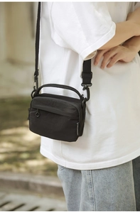Detail of a compact black crossbody bag with adjustable straps and front zip pocket