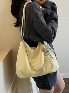 Minimalist pale yellow tote bag with metal chain and plush charm shown on model
