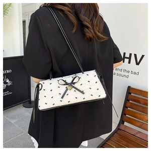 Detail view of a white ruched shoulder bag with black bow prints and heart pendant