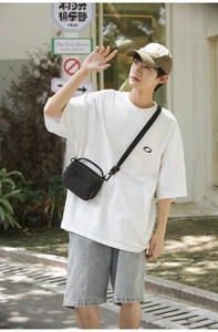 Outdoor shot of a black nylon crossbody bag with adjustable strap and front zipper pocket