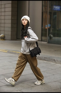 Outdoor street view of a black messenger bag with flap and dual buckle closures