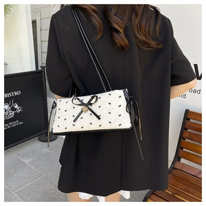 Chic white quilted shoulder bag with black bow patterns and a gold heart pendant charm