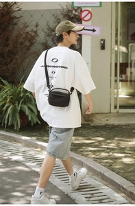 Outdoor street view showing the size and scale of the black crossbody bag worn by a model
