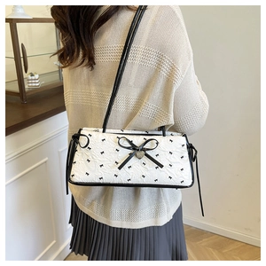 Detailed view of white quilted shoulder bag with black bows and silver heart pendant