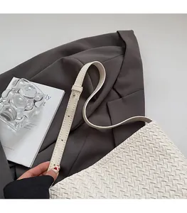 Detailed close-up of a white woven bucket bag with adjustable shoulder strap and metal rivets