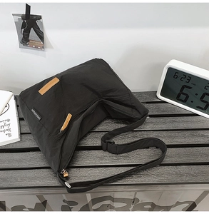 Detail of water-resistant black nylon messenger bag featuring adjustable strap and logo