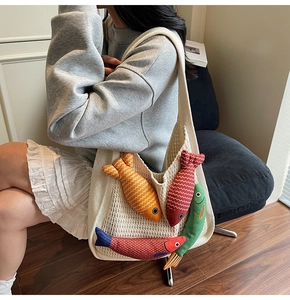 Detail of knitted cream tote bag with colorful 3D plush fish charms on textured surface