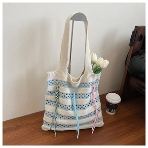 Detail of knitted striped tote bag with colorful braided ropes on a minimalist metal stand