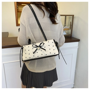 Detail of white textured shoulder bag with black bows and golden heart pendant