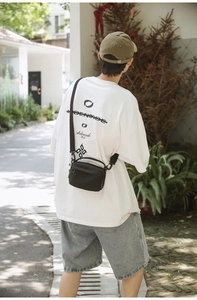 Rear view of model wearing a black nylon crossbody bag with oversized white graphic T-shirt