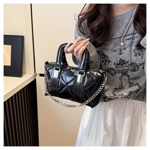 Close-up of black quilted shoulder bag with silver chain strap and shiny faux leather