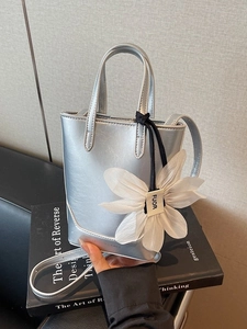 Mini sac cabas argenté avec breloque fleur et bandoulière sur fond de livre d'art