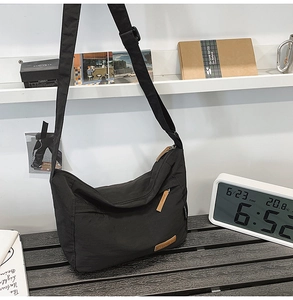 Detail of a black nylon messenger bag with brown leather accents on a wooden table