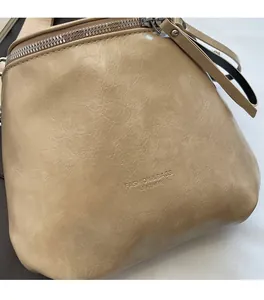 Close-up of soft genuine leather texture and embossed logo on minimalist beige crossbody bag
