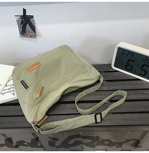 Detail of light green waterproof nylon messenger bag with orange leather logo on wooden table