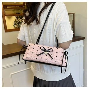 Pink bow shoulder bag with textured fabric, black bow details, and golden heart pendant
