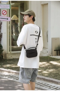 Detail of a black nylon crossbody bag worn with a white T-shirt and grey shorts