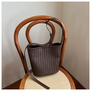 Detailed view of dark brown woven leather bucket bag texture and adjustable strap on a chair