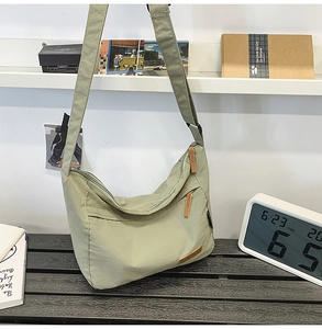 Detail of sage green nylon crescent bag with adjustable strap on a wooden bench