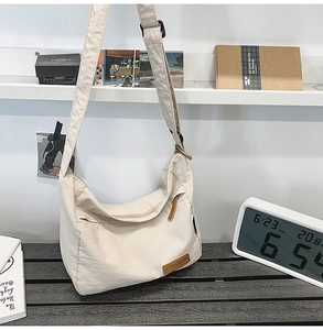 Detail of the minimalist beige nylon messenger bag with smooth zipper and leather logo
