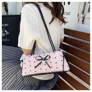 Pink bow shoulder bag with pleated texture and silver heart charm in outdoor setting