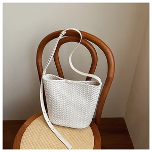 Detailed view of white woven bucket bag with V-shaped texture on a vintage wooden chair
