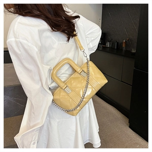 Detail of yellow quilted patent leather bag with silver chain strap on model in white dress