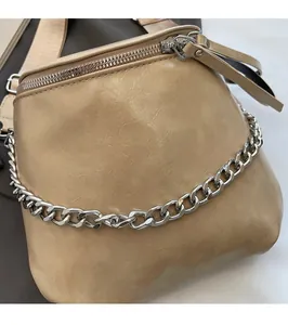 Close-up of pebble grain leather texture with metallic chain on a beige crossbody bag