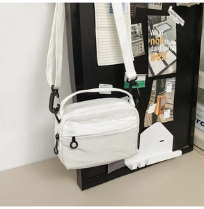Detail showing cream plaid crossbody bag with ripstop texture and adjustable black strap
