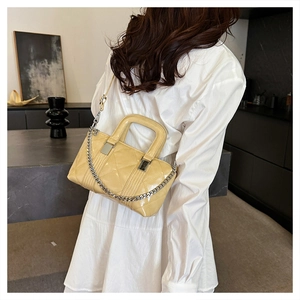 Close-up of beige quilted leather handbag with glossy finish and silver metal chain strap