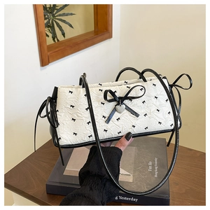 Detail of white textured shoulder bag with black bow prints and silver heart pendant