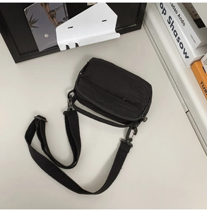 Detail of minimalist black nylon crossbody bag on a desk with artistic books