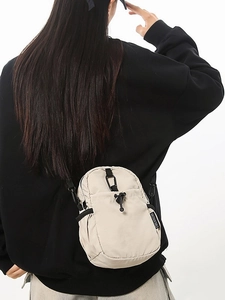 Sac bandoulière minimaliste en nylon beige imperméable porté par un mannequin sur fond blanc