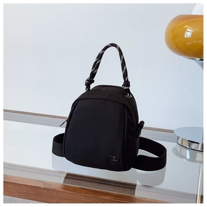 Detail of black nylon mini backpack with woven striped handle and silver metal logo