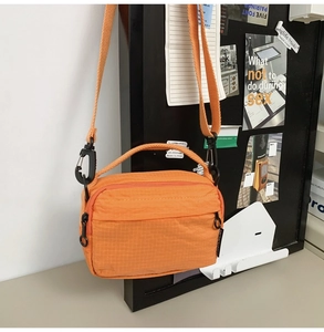 Detail of orange nylon crossbody bag with double zippers and black strap hooks