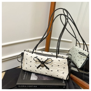Detail of white quilted handbag with black bow patterns and gold heart charm detail