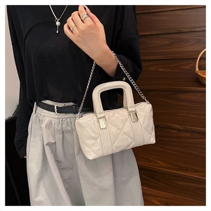 Close-up of quilted cream pillow bag with silver chain strap and metal zipper detail