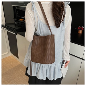 Détail d'un sac seau tressé marron foncé porté par un mannequin dans une cuisine épurée