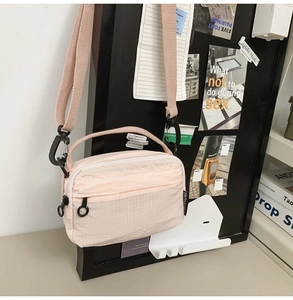 Detail of light pink waffle texture crossbody bag with zipper pockets and logo