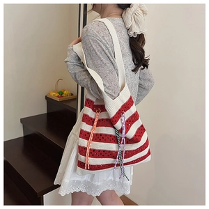 Close-up of red and white striped knit tote bag with tassel details and hollow patterns