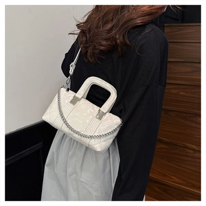 Rear view of model wearing a white quilted patent leather handbag with silver chain